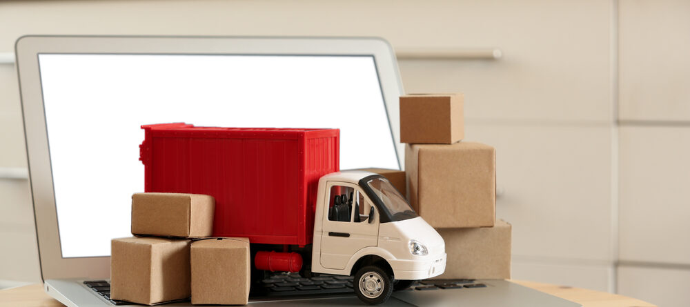 Laptop and truck model with boxes on table indoors. Courier service